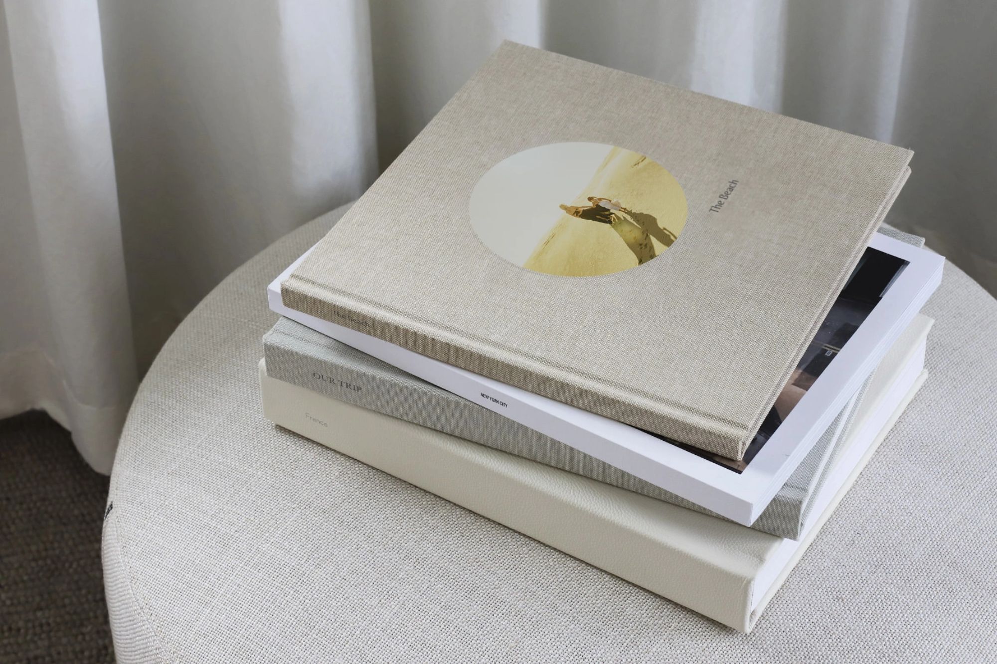 Stack of family photo albums on beige linen ottoman.