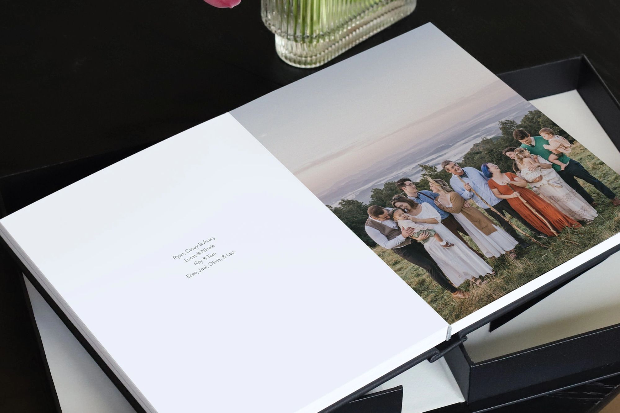 Black Portrait Premium Photo Album with family photo inside spread, laying on a black Presentation Box.