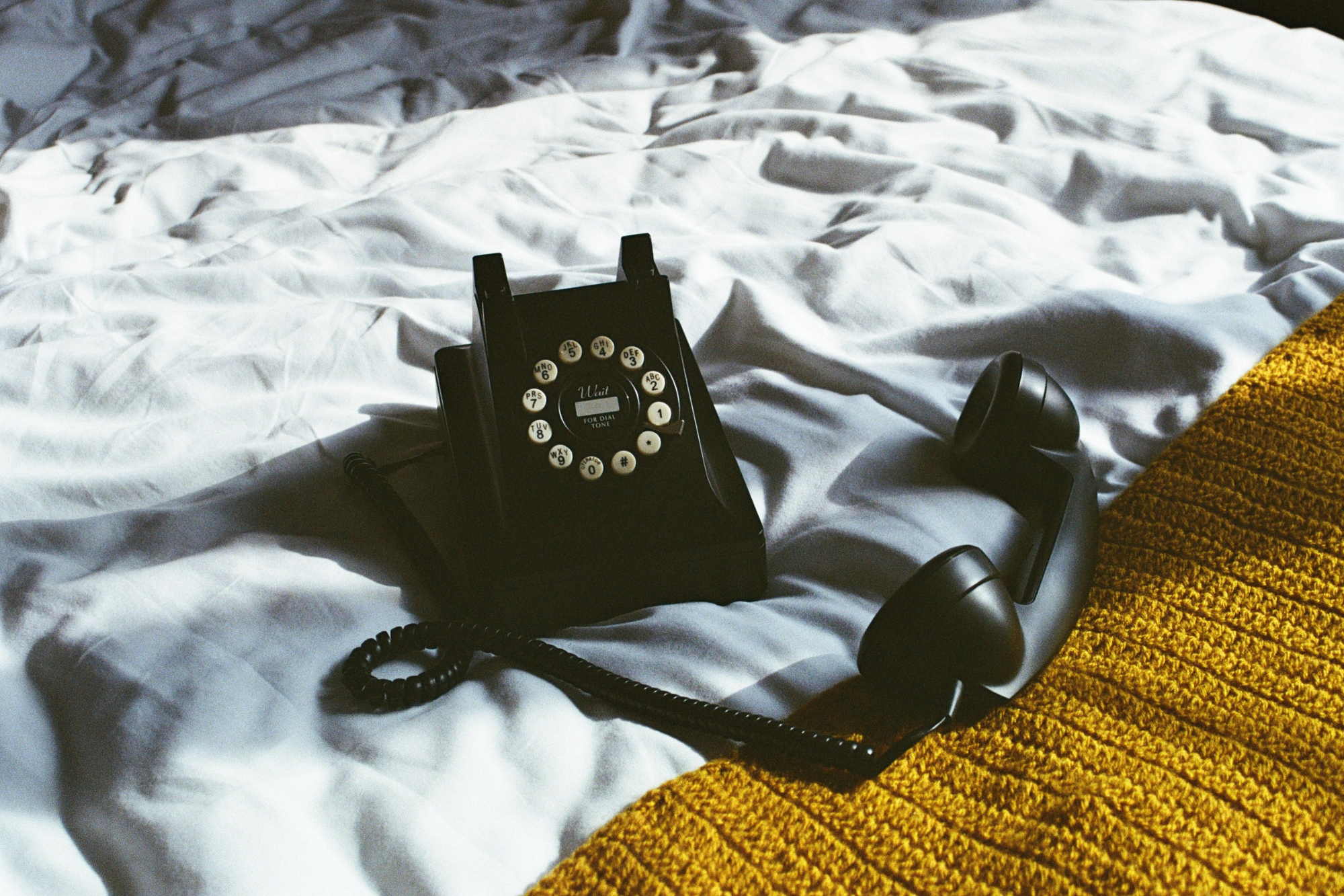 Vintage black rotary phone on bedsheets with yellow knit blanket