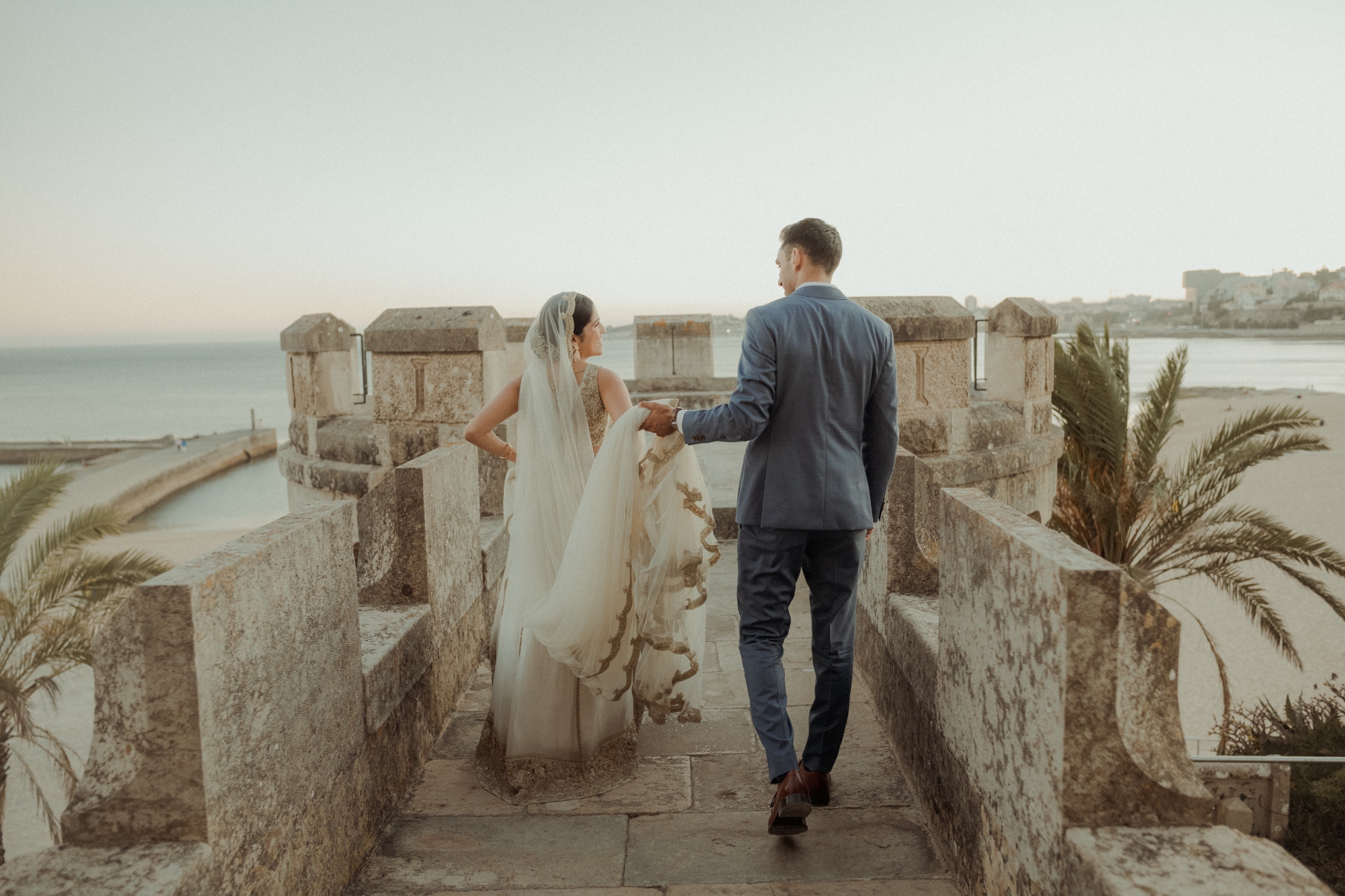 Bride and groom walking down arch with groom holding vail